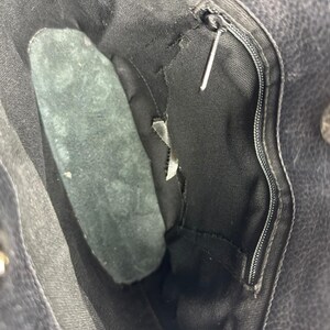 May include: Close-up of the interior of a black leather handbag. The bag features a zippered pocket, a magnetic snap closure, and a dark green suede insert. The interior lining is black.