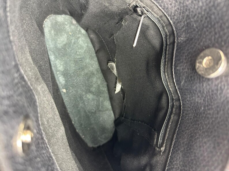 May include: Close-up of the interior of a black leather handbag. The bag features a zippered pocket, a magnetic snap closure, and a dark green suede insert. The interior lining is black.