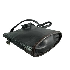 May include: Black leather backpack purse with a top handle and adjustable shoulder strap. The purse has a zipper closure with a decorative charm. The edges are trimmed with a brown leather. The bag is rectangular with rounded corners.