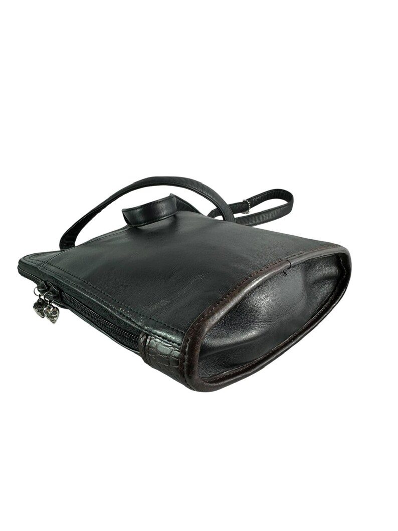 May include: Black leather backpack purse with a top handle and adjustable shoulder strap. The purse has a zipper closure with a decorative charm. The edges are trimmed with a brown leather. The bag is rectangular with rounded corners.