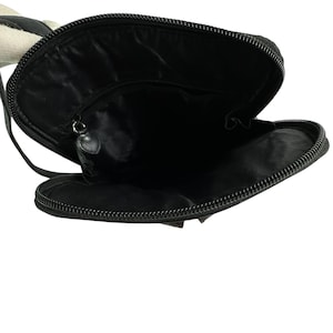 May include: Black crossbody bag with a zippered closure, open to reveal the interior. The bag has a black strap and a black zipper. The interior is black. The bag is made of a smooth material.
