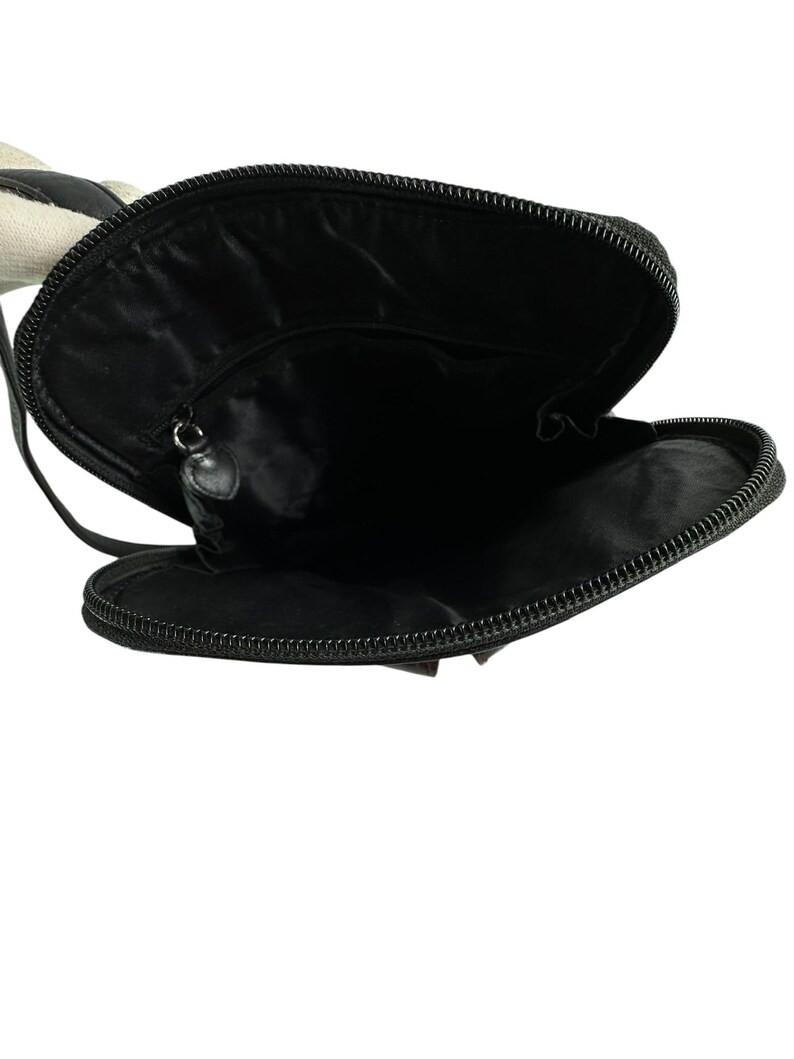 May include: Black crossbody bag with a zippered closure, open to reveal the interior. The bag has a black strap and a black zipper. The interior is black. The bag is made of a smooth material.