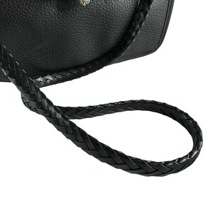 May include: Black leather handbag with a braided strap. The bag features a silver-toned clasp with a gold heart accent. The leather has a textured appearance, and the strap is looped.