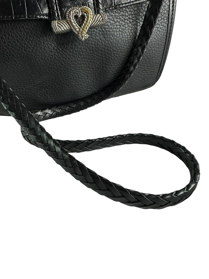 May include: Black leather handbag with a braided strap. The bag features a silver-toned clasp with a gold heart accent. The leather has a textured appearance, and the strap is looped.