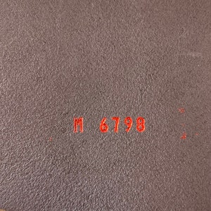 May include: Close-up of a brown leather belt with the text "M 6798" embossed in red.
