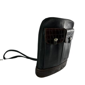 May include: Black leather crossbody bag with two front pockets featuring a brown crocodile-textured design. The bag has a long black strap and a brown crocodile-textured base. Silver-toned hardware accents the pockets.