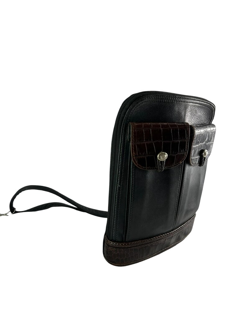 May include: Black leather crossbody bag with two front pockets featuring a brown crocodile-textured design. The bag has a long black strap and a brown crocodile-textured base. Silver-toned hardware accents the pockets.