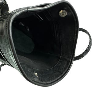 May include: Black leather handbag with a textured crocodile pattern. The interior is black with a small zippered pocket. The bag has a braided handle and a magnetic closure.