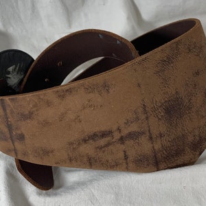 May include: A brown leather belt with a large, round, black buckle. The belt is distressed and has a worn look.