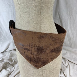 May include: A brown leather belt with a distressed finish and a large, round buckle. The belt is worn on a mannequin.