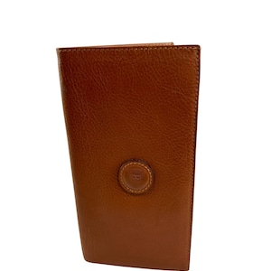 May include: A brown leather wallet with a textured surface. The wallet has a round emblem on the front and is closed. The wallet is rectangular and appears to be new.