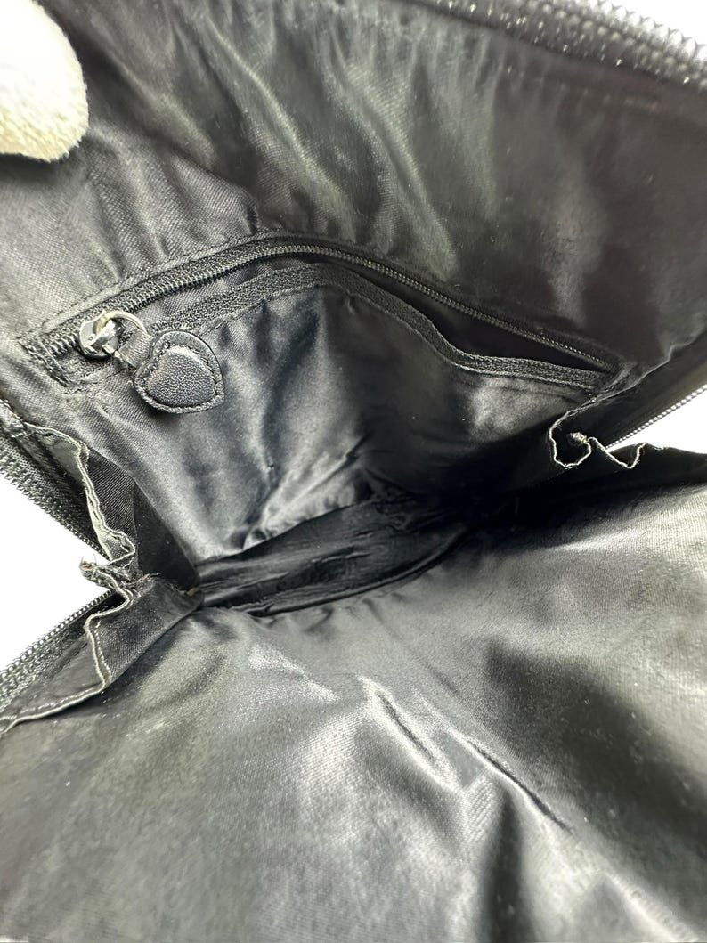 May include: Black nylon bag interior with multiple compartments and a zippered closure. The bag features a heart-shaped zipper pull and a smooth, shiny texture. The interior is designed for organization and storage.
