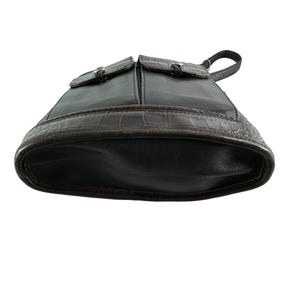 May include: Black leather backpack with two front pockets and silver-tone hardware. The bottom of the bag features a brown, textured, crocodile-like design. The bag has a top handle and adjustable straps.