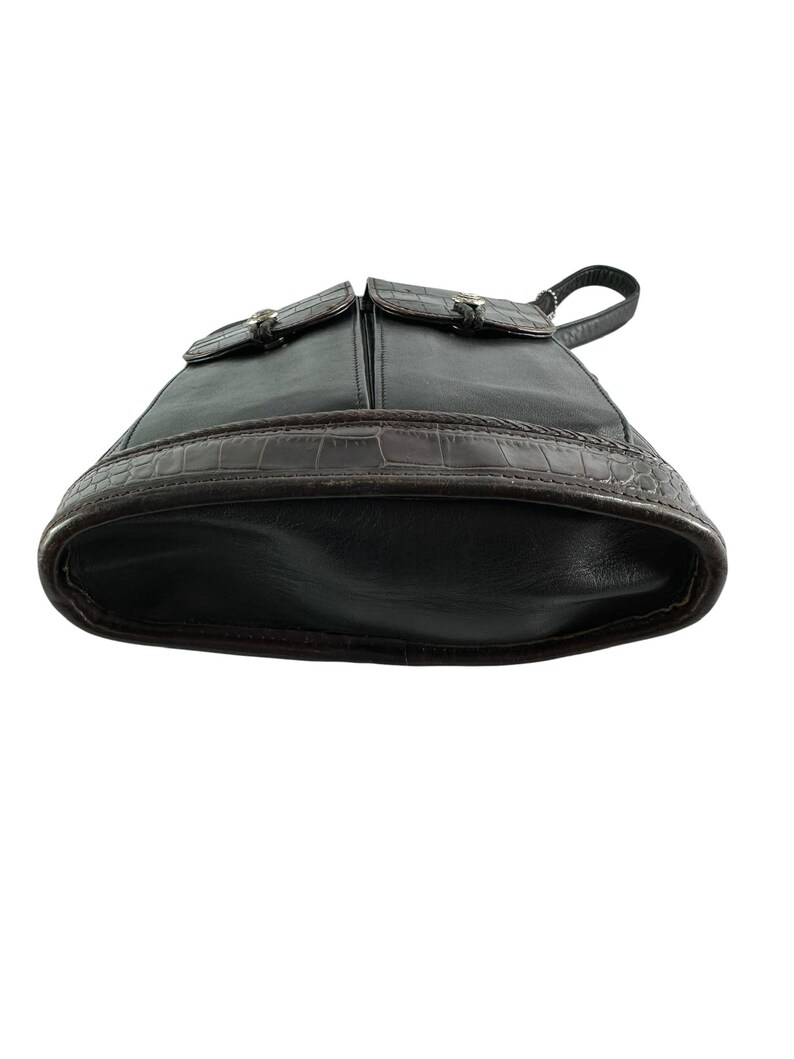 May include: Black leather backpack with two front pockets and silver-tone hardware. The bottom of the bag features a brown, textured, crocodile-like design. The bag has a top handle and adjustable straps.