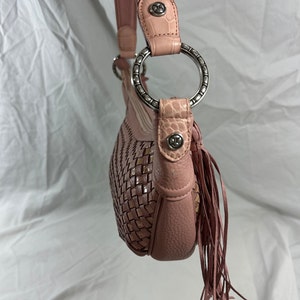 May include: A pink shoulder bag with a woven design on the front. The bag features a leather strap with silver metal rings and decorative fringe. The strap has a light brown crocodile-textured leather accent.