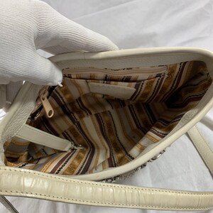 May include: A white leather handbag with a silver chain strap and a striped fabric lining. The bag has a zipper closure and a small pocket on the inside.
