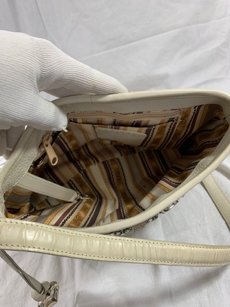 May include: A white leather handbag with a silver chain strap and a striped fabric lining. The bag has a zipper closure and a small pocket on the inside.