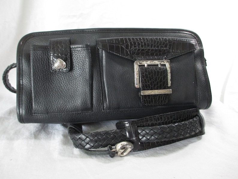 May include: Black leather handbag with a braided strap and a silver buckle. The bag has multiple pockets and a crocodile embossed detail.