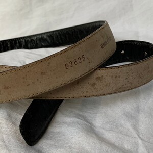 Op de afbeelding: Een bruine leren riem met een zwarte leren achterkant. De riem heeft het nummer "62625" erop gestempeld.