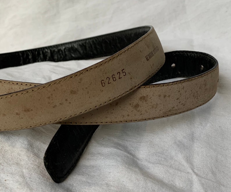 Op de afbeelding: Een bruine leren riem met een zwarte leren achterkant. De riem heeft het nummer "62625" erop gestempeld.