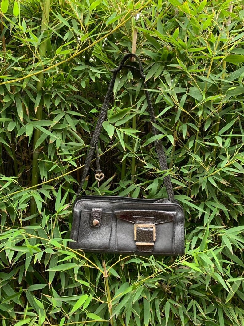 May include: A black leather shoulder bag with a gold buckle and a small heart charm. The bag has a braided strap and multiple pockets.