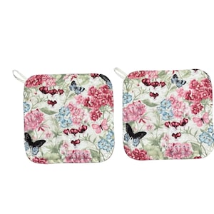 May include: Two square pot holders with a floral and butterfly pattern. The design features pink and blue flowers, green leaves, and butterflies in various colors. Each pot holder has a white loop for hanging.