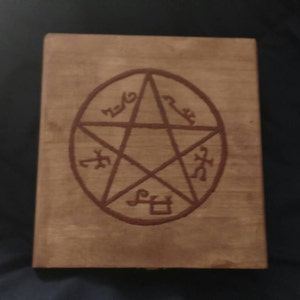 May include: A wooden journal with a brown pentagram symbol on the front. The symbol is surrounded by five runes, each with a different design.