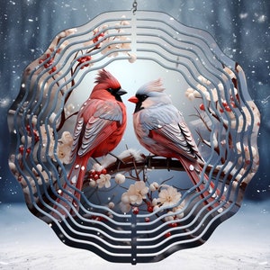 May include: A metal wind spinner with a winter theme features two cardinals perched on a branch with white blossoms and red berries. The spinner has a blue and silver design with a swirling pattern.