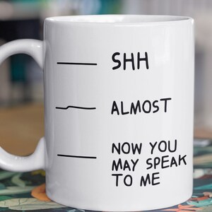 May include: White ceramic mug with black text that reads "Shh - Almost - Now you may speak to me".