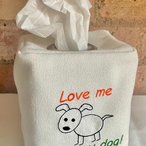 May include: White fabric tissue box cover with a cartoon dog embroidered on the front. The text "Love me" is in red above the dog, and "Love my dog!" is in green below. White tissues are pulled from the top.