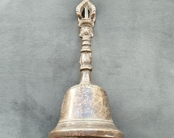 May include: A detailed, antique-style bell with a decorative handle and ornate top. The bell is made of a tarnished metal, likely bronze or brass, and features intricate carvings. The bell's shape is traditional, with a flared base and a long handle.