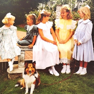 Könnte beinhalten: Fünf junge Mädchen in Vintage-Kleidern und weißen Schleifen sitzen auf einer Steinbank in einem Garten. Ein Sheltie-Hund sitzt auf dem Rasen vor ihnen. Die Mädchen tragen Kleider in Blau, Gelb, Weiß und Grau mit weißen Socken und Schuhen.