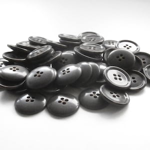 May include: A pile of grey plastic buttons with four holes each. The buttons are smooth and shiny.