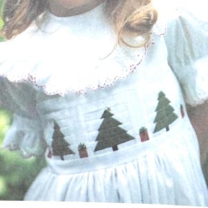 Könnte beinhalten: Weißes Kleid mit Rüschenkragen und Ärmeln. Das Kleid hat gestickte Weihnachtsbäume und Geschenkboxen über dem Oberteil. Der Kragenbesatz ist rot.