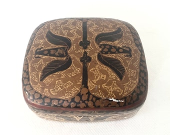 May include: A rectangular wooden box with a brown and gold patterned design. The box has a lid and is decorated with intricate floral motifs.