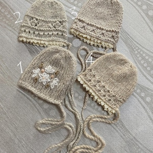 Puede incluir: Cuatro gorros de punto beige con lazos, numerados del uno al cuatro. El gorro uno presenta un bordado floral blanco. Los gorros dos, tres y cuatro muestran distintos patrones de punto texturizado y un borde de encaje color crema.