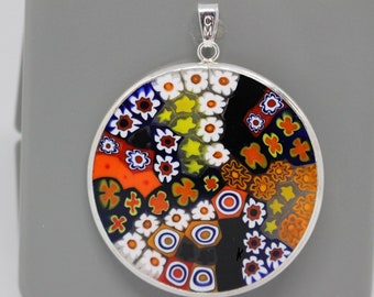 May include: A round silver pendant with a colorful Murano glass design. The glass features a mosaic of flowers, swirls, and geometric shapes in shades of orange, blue, white, black, and yellow.