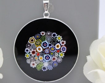 May include: A round silver pendant with a black background and a colorful millefiori glass design. The glass design features a variety of small, colorful flowers and geometric shapes.