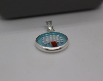 May include: A silver pendant with a blue and white enamel design. The design features a white tree with red roots and a circle of white stars around it.