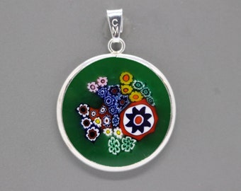 May include: A silver pendant with a round green glass charm featuring a colorful floral design. The charm has a silver border and a silver bail.