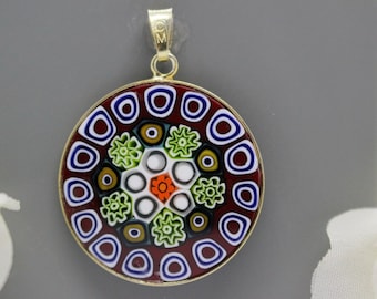 May include: A round pendant with a colorful, intricate design. The pendant is made of glass and has a gold-colored metal bail. The design features a central circle surrounded by concentric rings of different colors and patterns.