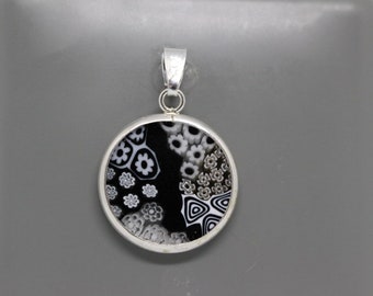 May include: A silver pendant with a round black and white glass charm featuring a geometric pattern. The charm is set in a silver frame.