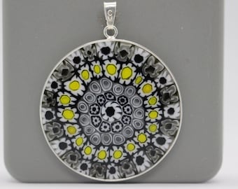 May include: A silver pendant with a round, black, white, and yellow glass design. The glass design features a circular pattern with concentric circles and small dots.
