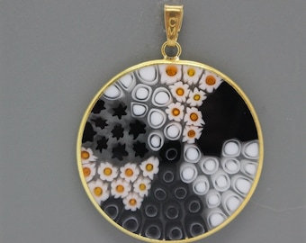 May include: A round pendant with a gold frame and a black, white, and orange glass design. The design features a swirling pattern of circles, stars, and flowers.