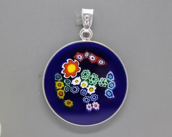 May include: Round pendant with a dark blue background and a floral design in various colors. The pendant has a silver-colored metal frame and bail. The floral design includes yellow, orange, white, green, and blue flowers.