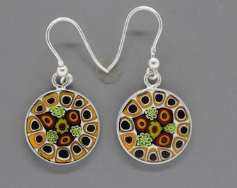 May include: A pair of silver earrings with round, colorful glass pendants. The pendants feature a circular pattern of yellow, orange, red, green, and black glass.