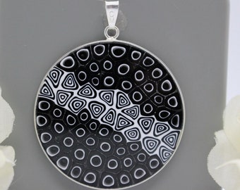 May include: A silver pendant necklace with a round black and white glass charm featuring a geometric pattern of circles and triangles.