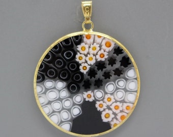 May include: A round pendant with a gold frame and a colorful glass design. The design features black, white, and orange colors in a geometric pattern.