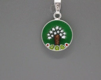 May include: A silver pendant with a round green glass charm featuring a white tree with a brown trunk and a green and white border.