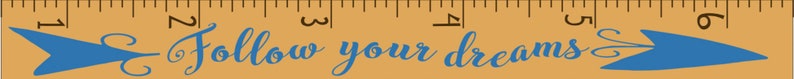 May include: A wooden ruler with inch markings and the phrase "Follow your dreams" in blue script. Blue arrow designs flank the text, adding a decorative touch to the inspirational message.